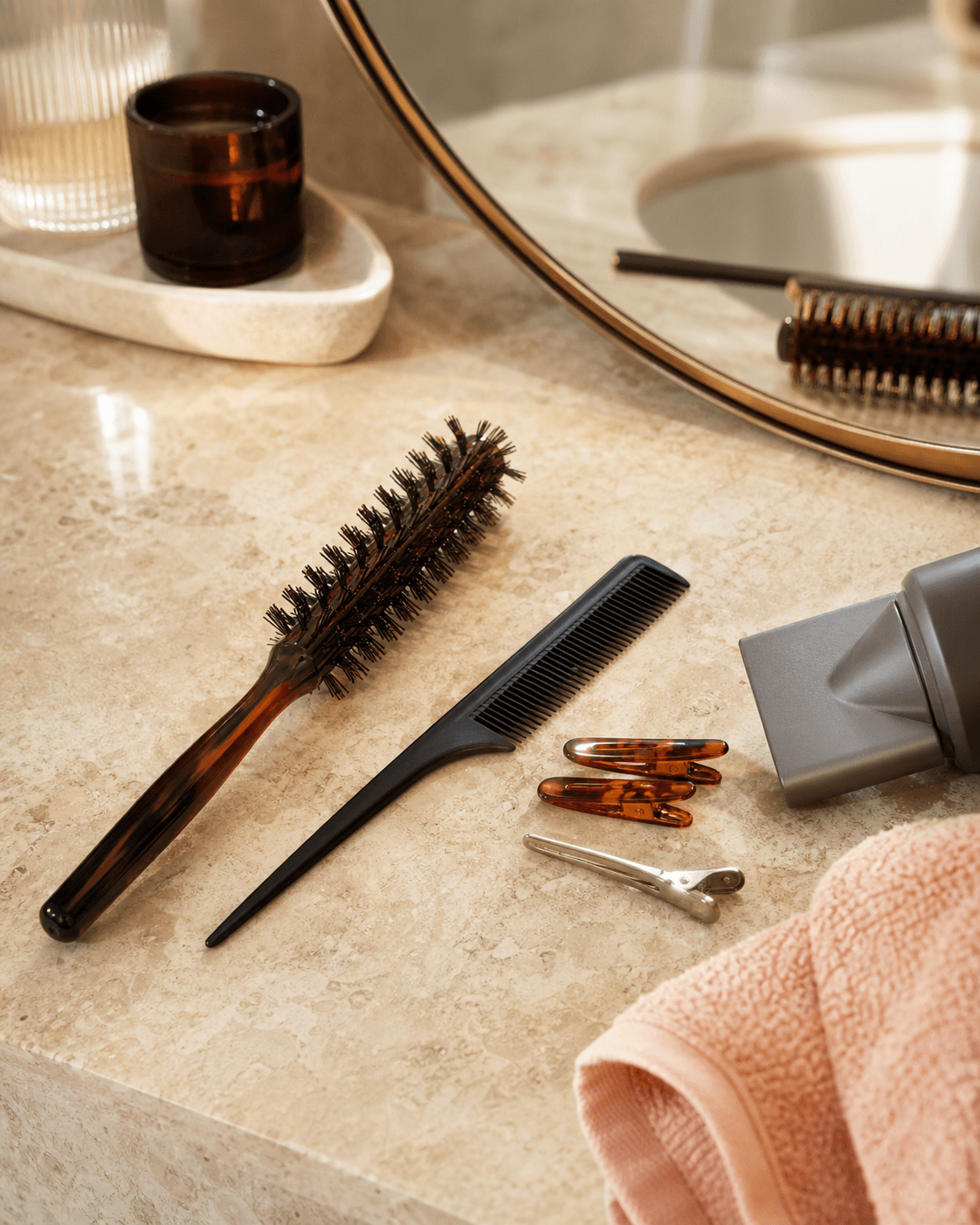 A bathroom vanity with a round brush, comb, clips, and peach towel.